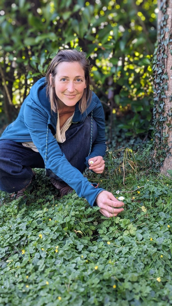 Guillemette Huet de Froberville cueillant des pâquerettes au pied d'un arbre